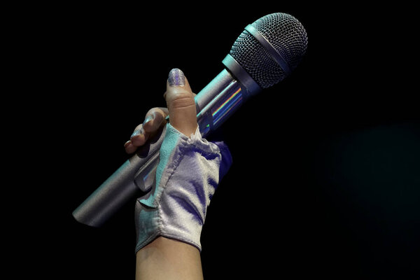 A woman in a leather glove holding a big silver wireless microphone for singing isolated on black  background. Rock star with beautiful manicure singing. no face. 