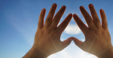 Kalp sembolü gökyüzü arka planındaki eller, Aşk ya da Sağlık kavramı. Kavramsal insan, erkek ya da kadın, birbirine aşık, sevgililer günü şekli ya da mavi gökyüzü arka planındaki kalp sembolü.