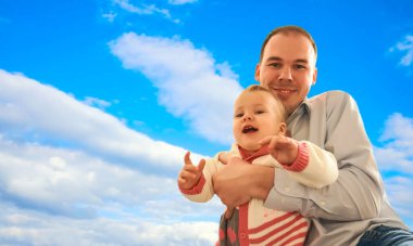Babasının kızı. Güçlü babası olan çocuk elleri mavi bulutlu arka planda. Mutlu bir baba ve sevimli küçük kızının portresi. Babalar günün kutlu olsun..