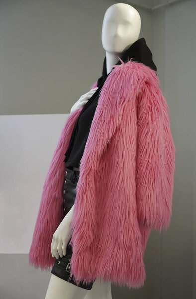A mannequin in a shop window in a winter coat made of pink faux fur and  black hoodie on his body. Fashionable concept of autumn or winter clothes for women 