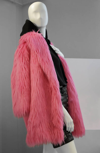 A mannequin in a shop window in a winter coat made of pink faux fur and  black hoodie on his body. Fashionable concept of autumn or winter clothes for women