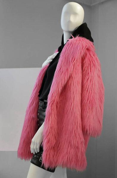 A mannequin in a shop window in a winter coat made of pink faux fur and  black hoodie on his body. Fashionable concept of autumn or winter clothes for women