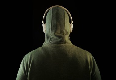 Kapüşonlu, beyaz kulaklıklı, tanınmayan bir adam. Geriye, dikiz aynasına. Siyah arka planda izole edilmiş. yüksek sesli müzik