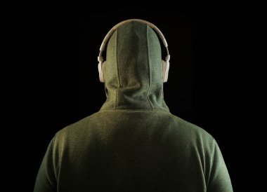 Kapüşonlu, beyaz kulaklıklı, tanınmayan bir adam. Geriye, dikiz aynasına. Siyah arka planda izole edilmiş. yüksek sesli müzik