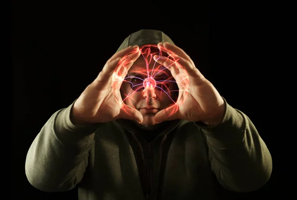 Energy ball in wizard hand. Bearded man casting bright magic ball spell. isolated on black background. portrait of a young adult man in a hood and in round  sunglasses. round frame made by hands