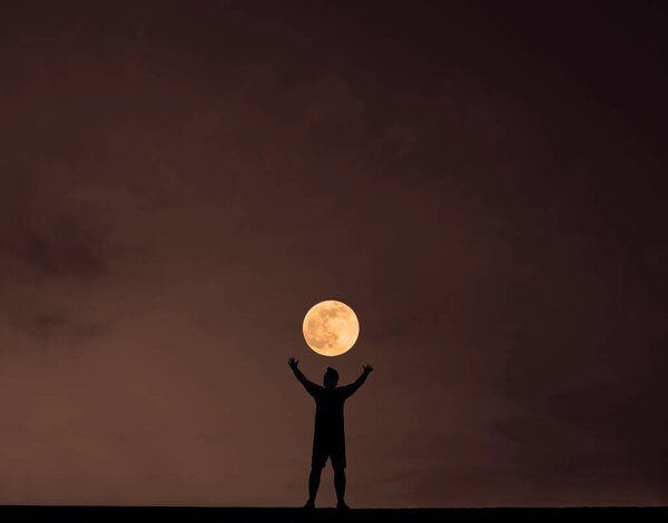 Silhouette of a young man with hands up against the night background. night scene.