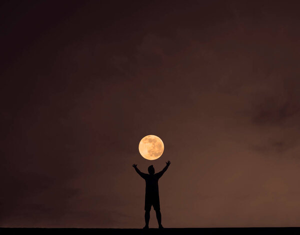 Silhouette of a young man with hands up against the night background. night scene.