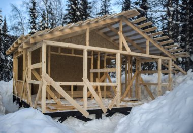 Kışları ahşap bir evin çatısı inşa edilir. Kış mevsimi. Karlı bir konutta inşaat halindeki kare çerçeveli ev. Vahşi orman. Kar yağdıktan sonra.