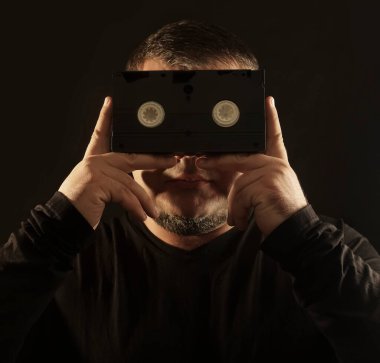 Elinde kaset tutan, video kasetin arkasına bakan, siyah arka planda izole edilmiş bir adam..