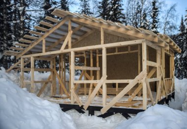 Kışları ahşap bir evin çatısı inşa edilir. Kış mevsimi. Karlı bir konutta inşaat halindeki kare çerçeveli ev. Vahşi orman. Kar yağdıktan sonra.