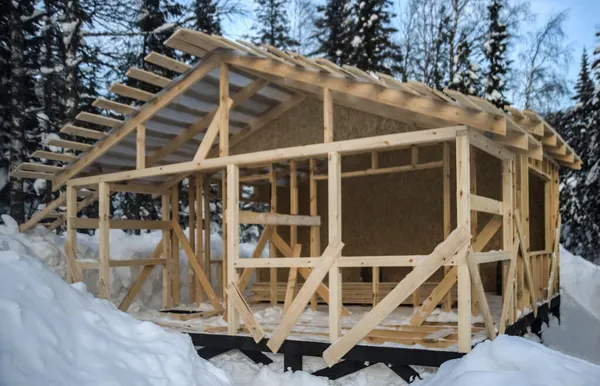 winter construction of a wooden house frame work roof. winter season. Square frame Home under construction on a snowy residential . wild forest. after snowfall.