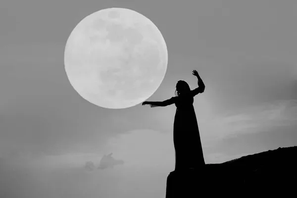 女性のシルエットが山の頂上に立っている 女性は森の木々の上で満月を手に持っている バックライトと月の光 いい振動だ — ストック写真