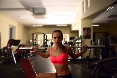 Spor salonunda bankta otururken halter çubuğuyla antrenman yapan kararlı bir kadın.