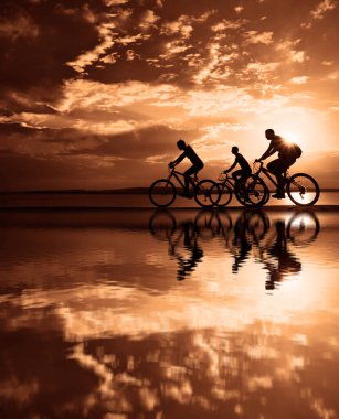 Boşluk. Gün batımında bisiklete binen sportif arkadaşlar. Bisikletçiler sahil boyunca gidiyor. Doğa arka planında spor.