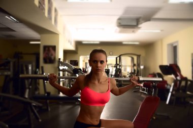 Spor salonunda bankta otururken halter çubuğuyla antrenman yapan kararlı bir kadın.