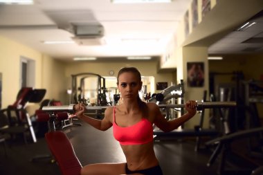 Spor salonunda bankta otururken halter çubuğuyla antrenman yapan kararlı bir kadın.