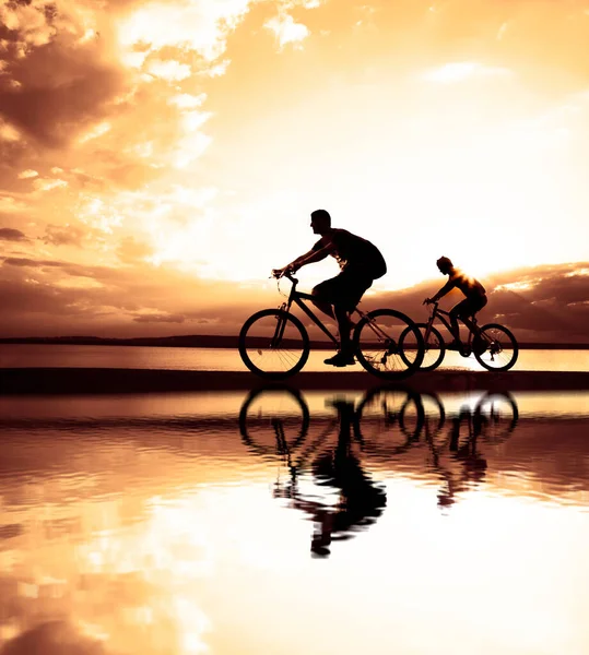 空荡荡的地方日落时骑自行车的朋友们 骑自行车的人沿着海岸骑行 大自然体育背景 — 图库照片