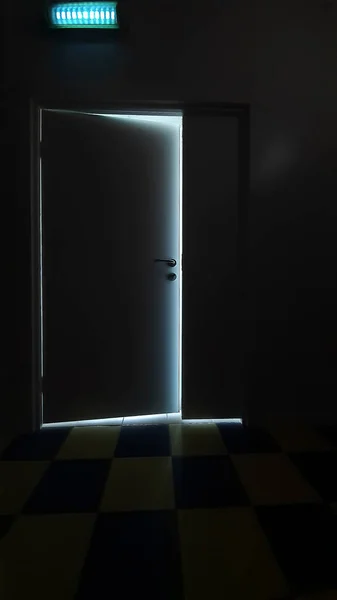 在黑暗的走廊尽头 一道微开的门缝隙中透出的流光代表着希望和机遇就在门的另一边 黑暗房间里的灯 打开的门 半开的门 — 图库照片