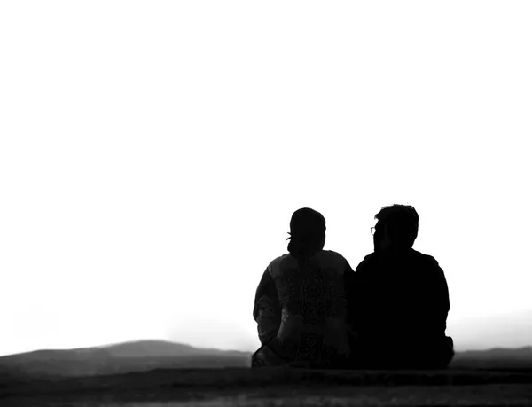シルエットの旅行者のカップルのバックビュー一緒に座って 背景に空と山の上に美しい日の出や日没を見て 月を見ている男と女 — ストック写真