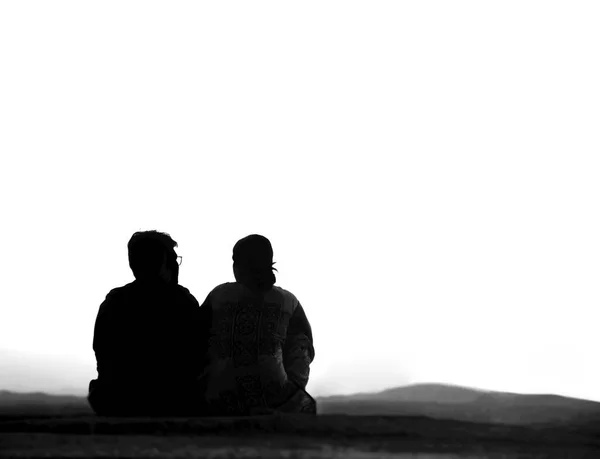 シルエットの旅行者のカップルのバックビュー一緒に座って 背景に空と山の上に美しい日の出や日没を見て 月を見ている男と女 — ストック写真