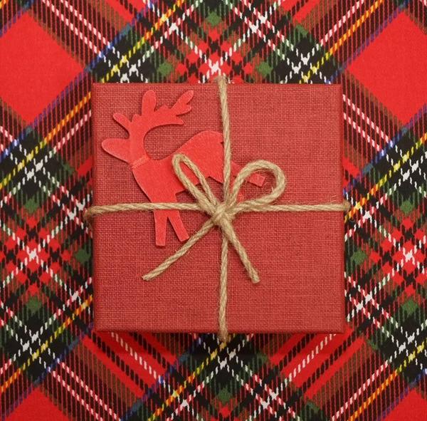 Ekose yün kumaş arka plan ve Noel hediyesi. Üst Manzara. Mutlu yıllar. İple bağlanmış bir hediye, kareli kırmızı masa örtüsü üzerinde.. 