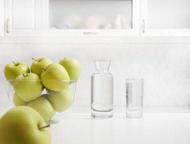 Mutfak masasında yeni yıkanmış elmalar. Dolapta bir şişe ve bir bardak su var. iç arkaplan. 