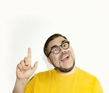 Gözlüklü mutlu genç adamın portresi beyaz arka planda izole bir şekilde duruyor, kameraya bakıyor, gülümsüyor ve yukarıda fotokopi alanında bir şeyler gösteriyor..