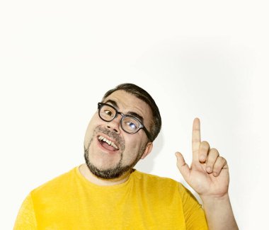 Gözlüklü mutlu genç adamın portresi beyaz arka planda izole bir şekilde duruyor, kameraya bakıyor, gülümsüyor ve yukarıda fotokopi alanında bir şeyler gösteriyor..