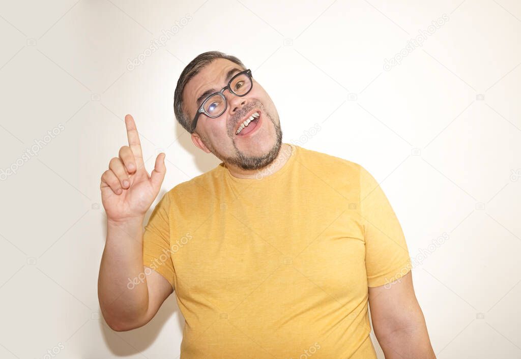 Portrait of happy positive cheerful young man in glasses standing isolated on white background, looking at camera, smiling and pointing up with finger  showing something on copy space above.