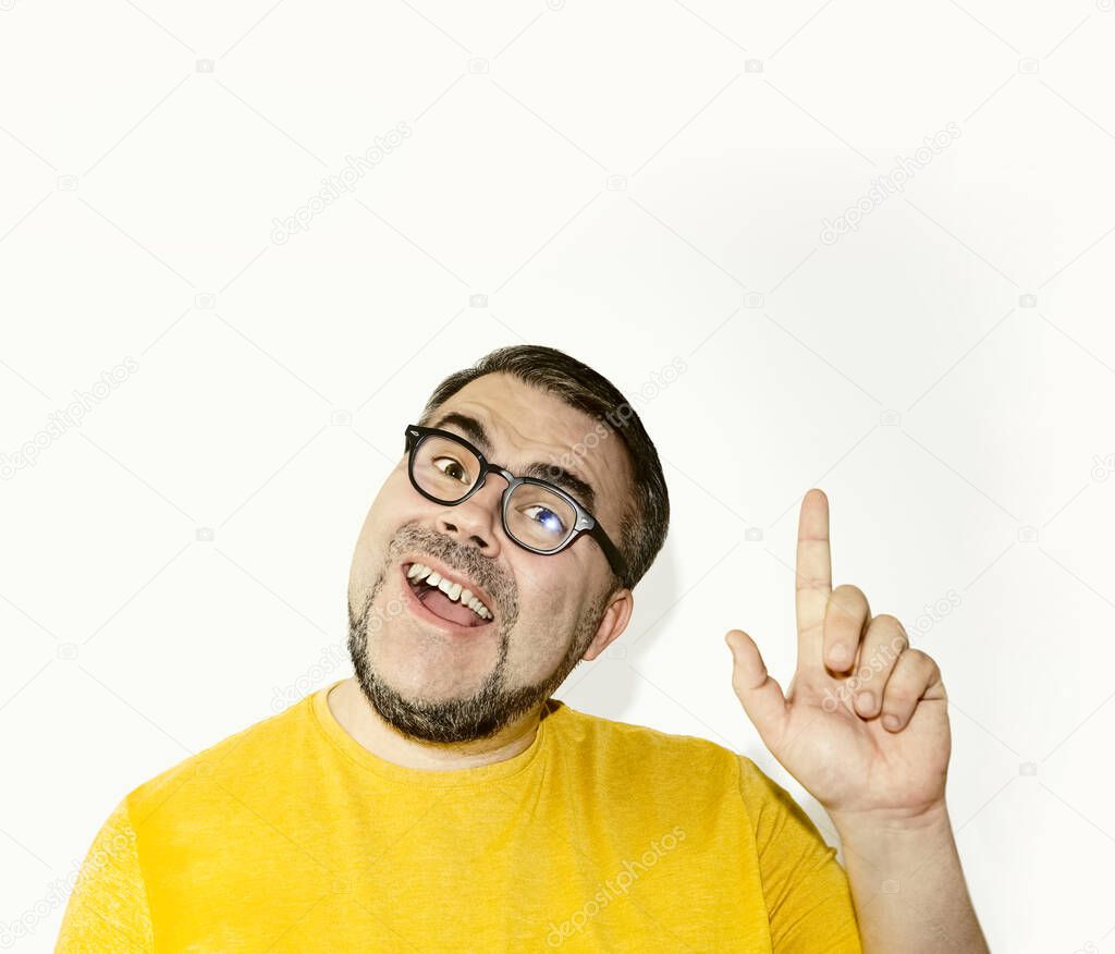 Portrait of happy positive cheerful young man in glasses standing isolated on white background, looking at camera, smiling and pointing up with finger  showing something on copy space above.