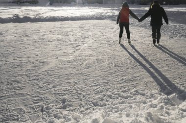 Genç çift dışarıda buz pateni yapıyor. Geriye, dikiz aynasına. Çift buz pateni pisti. Adam, aşık kadın kışlık giysiler giyip el ele tutuşuyorlar kadın erkek. tam uzunluk 