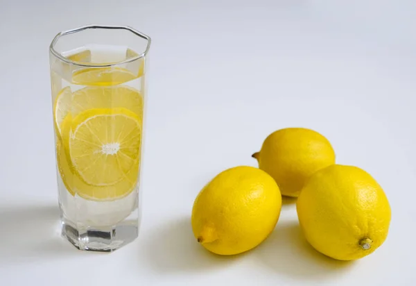 白いテーブルの上の透明なガラスの中に3つのレモンと純粋な飲料水 サイドビュー 白い背景に隔離され — ストック写真