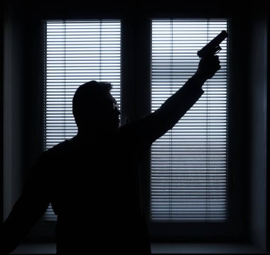A man with a gun is standing by the window blind, ready to protect himself from another bad people, crime scene conceptual. silhouette of an armed man behind blinds