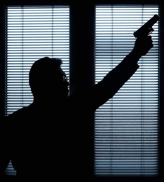 A man with a gun is standing by the window blind, ready to protect himself from another bad people, crime scene conceptual. silhouette of an armed man behind blinds