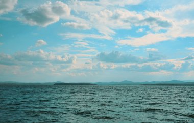 Idyllic boş kumsal ve dalgalı mavi deniz. Arkaplanda ada ve bulutlu gökyüzü. 