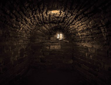 Eski mahzende gün ışığı parlıyor. Yeraltı kalesinde taş kemer. Elektrikli lamba ve parmaklıklı camlı eski taşlı hapishane. 