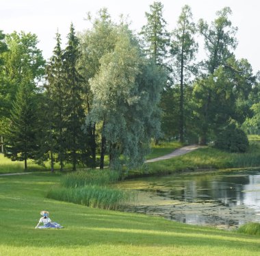 Bir yaz parkında çimlerde dinlenen elbiseli genç ve güzel bir kadın. arka, arka görünüm.