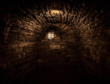 Eski mahzende gün ışığı parlıyor. Yeraltı kalesinde taş kemer. Elektrikli lamba ve parmaklıklı camlı eski taşlı hapishane. 