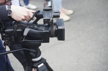 Genç kameraman ve video operatörü profesyonel kamerasıyla sokaktaki tripodunda röportaj yapıyor. Erkek gazeteci, operatör ve muhabir elinde video kamerayla sokakta çekim yapıyor. 