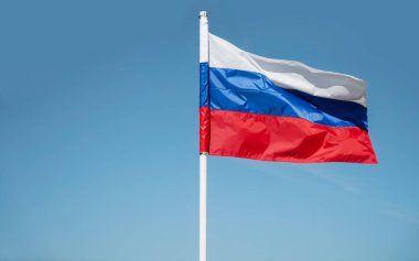 Üç renkli Rus bayrağı gökyüzüne karşı rüzgarda dalgalanıyor. Mavi gökyüzü arka planında Rus bayrağı