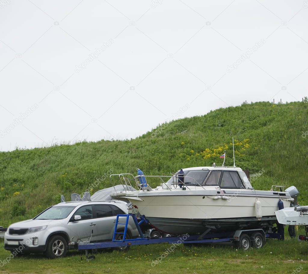 Car transporting  a big yacht or motor boat near green grass hill. 