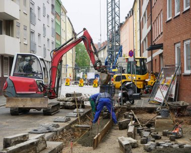 2 işçi ve kazıcının şoförü yaz mevsiminde araçlar ve yol ekipmanlarının yanı sıra çitler ve yol tabelalarıyla yolu onarıyor. Nuremberg, Almanya