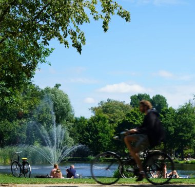 Amsterdam, Hollanda - 22 Temmuz 2019: Vondelpark dinlenme, yürüyüş yapan sakinler ve turistler için favori yer. Bisiklet süren adamın silueti..