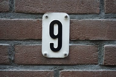 Hollanda Amsterdam 'daki 9 numaralı evi kapatın. 9 numaralı ev kırmızı tuğlalı duvarda, 9 numaralı beyaz metal plakalı.