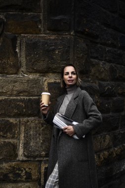 Orta yaşlı, gri ceketli, elinde moda dergisi ve kahve fincanı tutan bir kadın. Uzaklara bakan bir kadın.