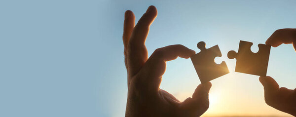 Две руки соединяют кусочки головоломки на фоне неба. Деревянная головоломка против солнечных лучей. Символ ассоциации и связи. Бизнес стратегия.