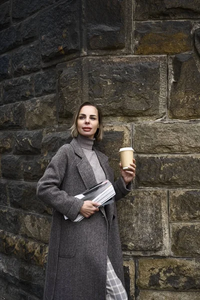 Frau Mittleren Alters Grauen Mantel Der Hand Modezeitschrift Und Kaffeetasse lizenzfreie Stockbilder