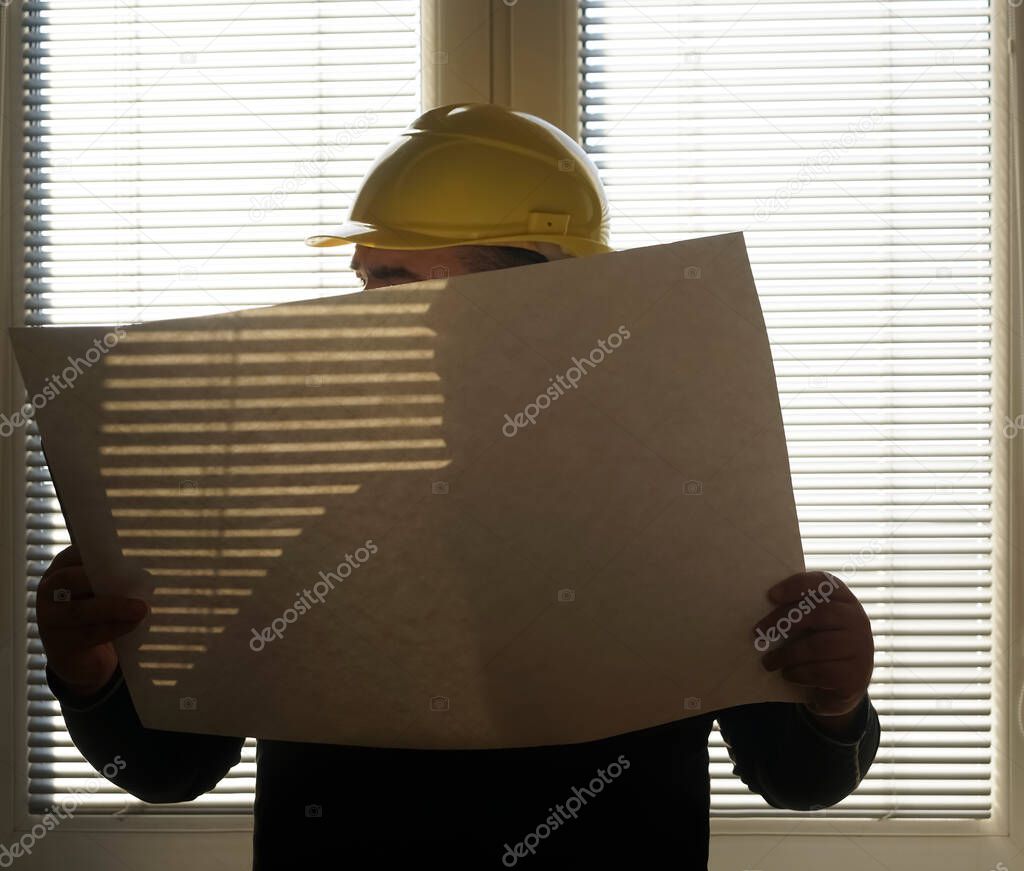 engineer wear yellow safety helmet with blue print is checking the under construction room and aluminum window frame. daylight through jalousie