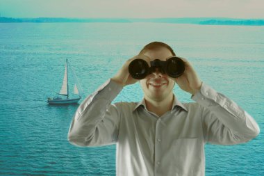 Uzun kollu gömlek giyen ve elinde dürbün tutan bir adam. Uzaklara bakıyor ve kıyıda duruyor. Okyanusu keşfeden genç bir iş adamı. Deniz ve mavi suyun arka planı.