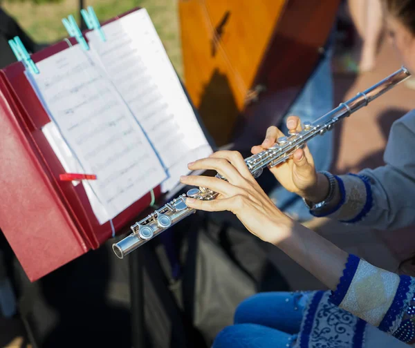 The girl is holding a large concert flute (in hands close-up). Professional musician at the rehearsal. A woman plays the transverse flute. closeup of hands of a musician playing the flute